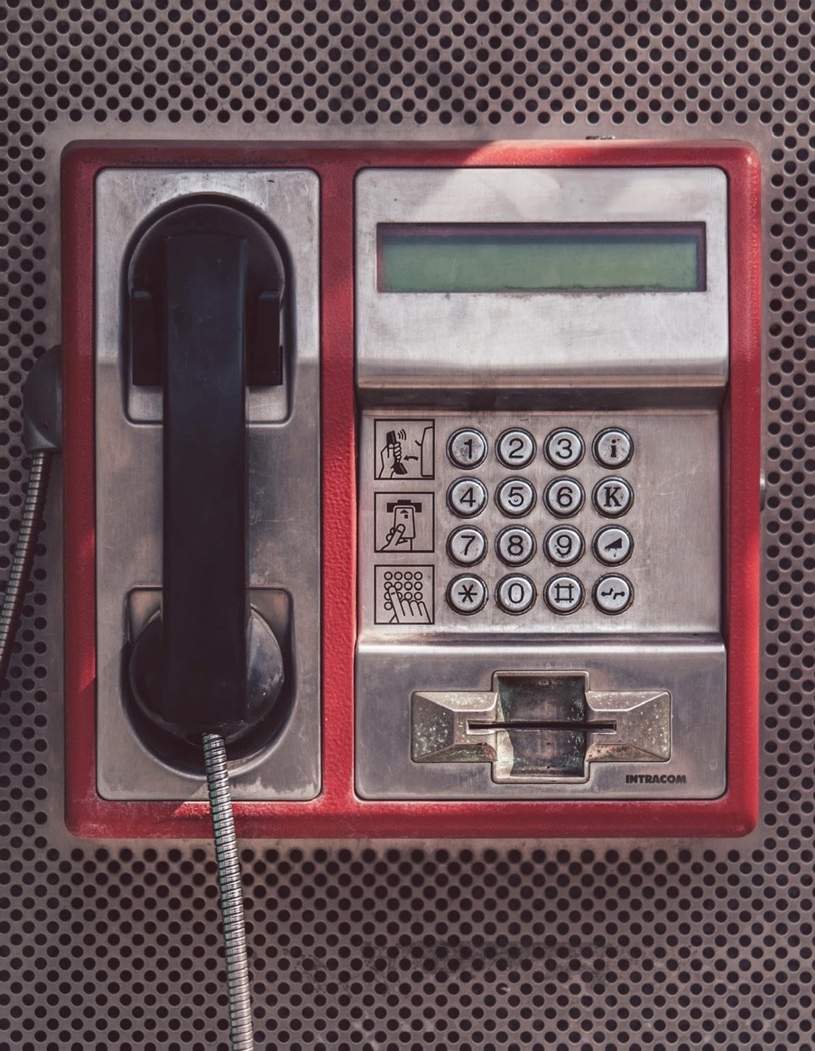 An old red analog payphone mounted on a metal wall